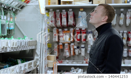 Customer browses a diverse range of light switches in a hardware store, weighing options for his upcoming home improvement project. A man in a hardware store, choosing sockets and switches. Customer browses a diverse range of light switches in a hardware store, weighing options for his upcoming home improvement project. A man in a hardware store, choosing sockets and switches. 140441253