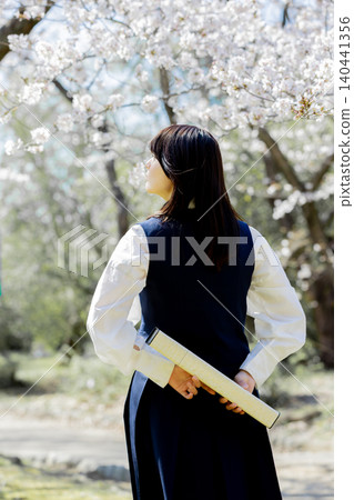A high school girl, with her graduation certificate in hand, gazes towards the future amidst a row of cherry trees. A high school girl, with her graduation certificate in hand, gazes towards the future amidst a row of cherry trees. 140441356