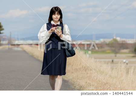 A high school girl walking to school while using her smartphone. A high school girl walking to school while using her smartphone. 140441544
