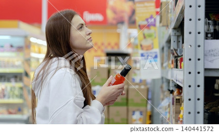 Young woman evaluates items during her supermarket visit, carefully comparing choices before making a purchase Young woman evaluates items during her supermarket visit, carefully comparing choices before making a purchase 140441572