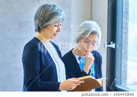 Senior women checking clipboards by the window Senior women checking clipboards by the window 140443840