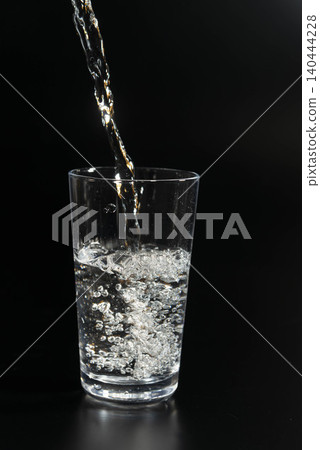 The moment light shines in a transparent glass filled with water against a black background. The moment light shines in a transparent glass filled with water against a black background. 140444228