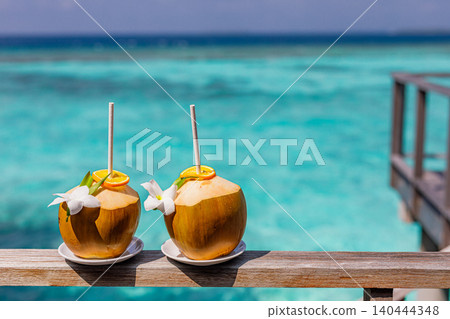 Tropical coconut beverage with straw over a dreamy ocean backdrop. Cool refreshing drink in bright summer sunlight. Relaxing peaceful vacation scene with happy holiday mood. Inspirational beach Tropical coconut beverage with straw over a dreamy ocean backdrop. Cool refreshing drink in bright summer sunlight. Relaxing peaceful vacation scene with happy holiday mood. Inspirational beach 140444348