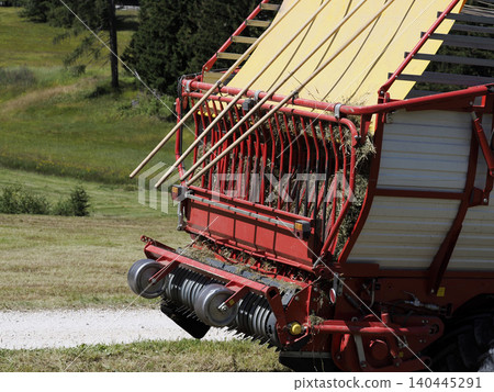 Red Forage Wagon Collecting Hay in a Sunny Farm Field During Harvest Season in dolomites Red Forage Wagon Collecting Hay in a Sunny Farm Field During Harvest Season in dolomites 140445291