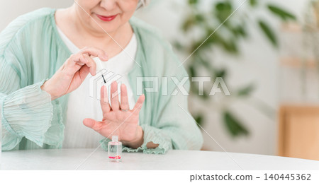 一位頭髮花白的老婦人正在塗抹指甲油和護甲油來滋潤指甲。 一位頭髮花白的老婦人正在塗抹指甲油和護甲油來滋潤指甲。 140445362