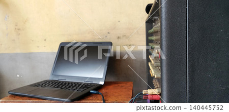 A laptop is placed on a wooden table next to an audio mixer or amplifier with cables connected. A laptop is placed on a wooden table next to an audio mixer or amplifier with cables connected. 140445752