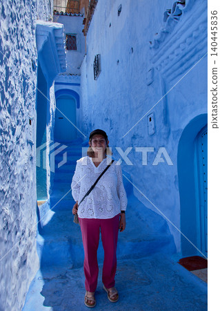 A female tourist poses smiling next to a blue wall decorated with flowerpots in the medina of Chefchaouen A female tourist poses smiling next to a blue wall decorated with flowerpots in the medina of Chefchaouen 140445836