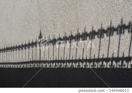 Shadow of an ornate wrought iron fence cast on asphalt surface Shadow of an ornate wrought iron fence cast on asphalt surface 140446013