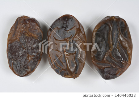 Three ripe Medjool dates lined up on a white background 140446028