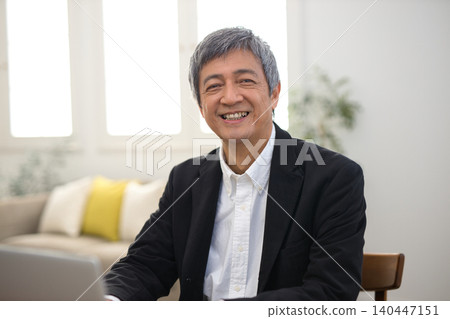 一位六十多歲的男子，穿著夾克，正在使用筆記型電腦。 140447151