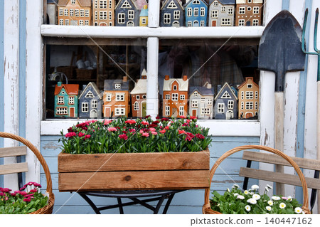 Shop window display of miniature houses and spring flowers with garden tools outside cottage store Shop window display of miniature houses and spring flowers with garden tools outside cottage store 140447162