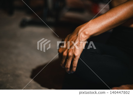 Close-up of a relaxed hand resting on the knee during meditation in a dark gym, symbolizing mindfulness, breathing, calm focus, yoga practice, wellness, recovery, and inner balance. Close-up of a relaxed hand resting on the knee during meditation in a dark gym, symbolizing mindfulness, breathing, calm focus, yoga practice, wellness, recovery, and inner balance. 140447802