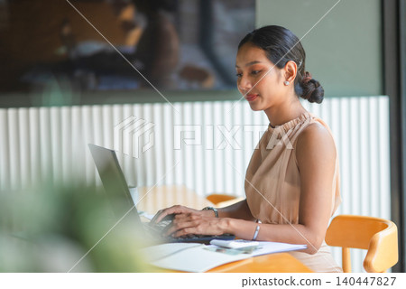Businesswoman typing on a laptop at an office desk with financial paperwork, highlighting digital work, accounting tasks, business planning, productivity, remote work, and data review. Businesswoman typing on a laptop at an office desk with financial paperwork, highlighting digital work, accounting tasks, business planning, productivity, remote work, and data review. 140447827