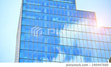 Modern office building with glass facade on a clear sky background. Transparent glass wall of office building. Modern office building with glass facade on a clear sky background. Transparent glass wall of office building. 140447880