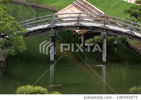 A wooden arched bridge and Nishikigoi (koi carp) spanning a pond in a Japanese garden. A wooden arched bridge and Nishikigoi (koi carp) spanning a pond in a Japanese garden. 140448075