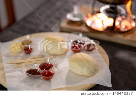 Preparing a burgundian fondue dinner featuring a pot of bubbling hot oil, accompanied by various bread rolls and small dishes of flavorful sauces on a wooden board Preparing a burgundian fondue dinner featuring a pot of bubbling hot oil, accompanied by various bread rolls and small dishes of flavorful sauces on a wooden board 140448357