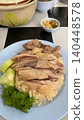 thai street food Sliced steamed chicken served over fragrant rice, garnished with cucumber and fresh cilantro, traditional Hainanese chicken rice dish, Asian comfort food on white ceramic plate., vert 140448578