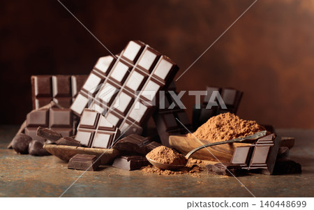 Scraps of dark chocolate next to a wooden bowl of cocoa powder. 140448699