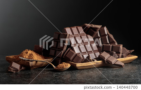 Broken dark chocolate bar and cocoa powder on a black background. 140448700