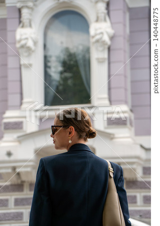 Young woman in sunglasses stands against ornate historic facade, decorative stucco details, elegant architectural elements. Luxury lifestyle, fashion, city branding, premium travel 140448775