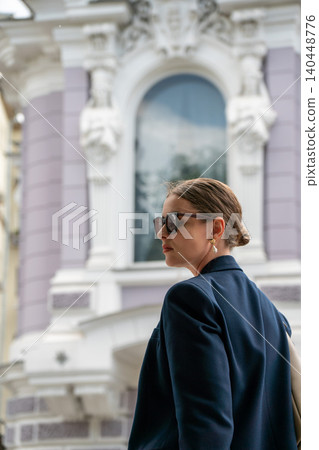 Young woman in sunglasses stands against ornate historic facade, decorative stucco details, elegant architectural elements. Luxury lifestyle, fashion, city branding, premium travel 140448776