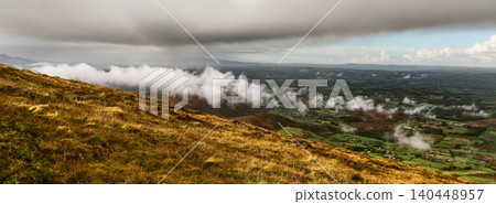 A view from a hillside shows a valley filled with mist and rolling hills in the distance. A view from a hillside shows a valley filled with mist and rolling hills in the distance. 140448957