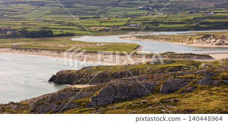 Numerous people enjoy a wide sandy beach, with some wading in the water. Numerous people enjoy a wide sandy beach, with some wading in the water. 140448964