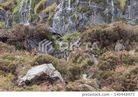 A small waterfall trickles down a dark, wet rock face on a rugged cliff. A small waterfall trickles down a dark, wet rock face on a rugged cliff. 140448975