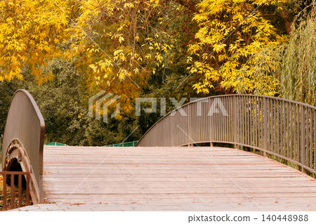 scenic view of a park bridge during the fall season, surrounded by trees displaying golden leaves and lush greenery scenic view of a park bridge during the fall season, surrounded by trees displaying golden leaves and lush greenery 140448988
