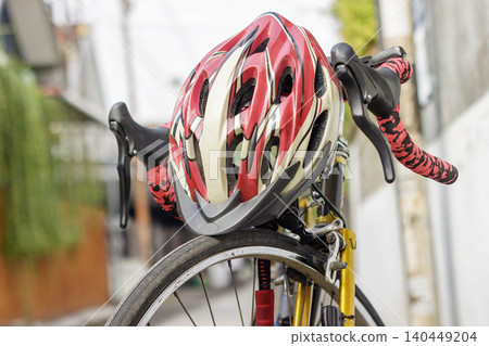 Dramatic close-up front view of a road bicycle showcasing the front wheel, brake caliper, pink patterned handlebar grips, and a red cycling helmet resting on top. High Quality Photo Dramatic close-up front view of a road bicycle showcasing the front wheel, brake caliper, pink patterned handlebar grips, and a red cycling helmet resting on top. High Quality Photo 140449204