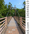 A suspension bridge in a park, against a blue sky and surrounded by lush green trees (vertical orientation) [Isokawa Green Park/Tochigi] 140449219