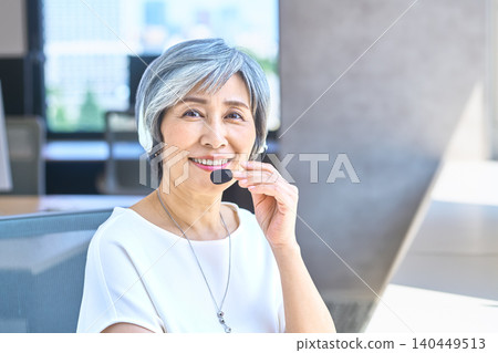 資深女接線生戴著耳機,手放在麥克風上講話。 資深女接線生戴著耳機,手放在麥克風上講話。 140449513