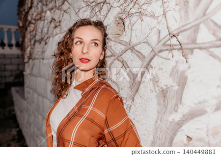 Woman portrait hair leaning against a rustic white wall wearing an orange plaid shirt in soft evening light 140449881