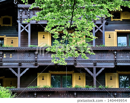 Wooden chalet facade with yellow shutters and leafy tree Wooden chalet facade with yellow shutters and leafy tree 140449954