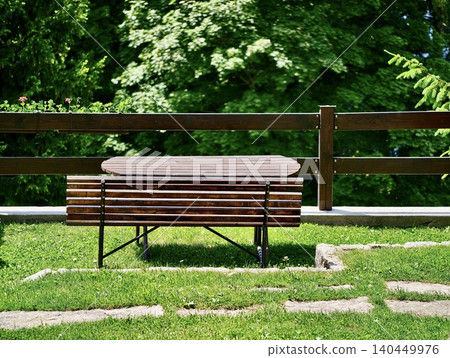 Wooden picnic table and bench on grassy terrace with leafy green backdrop Wooden picnic table and bench on grassy terrace with leafy green backdrop 140449976