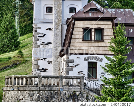 Stone and timber mountain lodge facade with balcony and fir tree 140450017