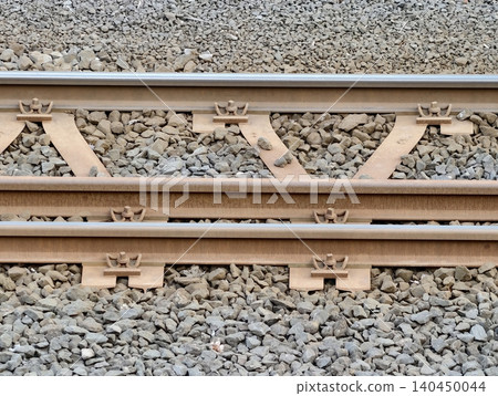 Close-up of rusted railway tracks and ballast with metal fastenings Close-up of rusted railway tracks and ballast with metal fastenings 140450044