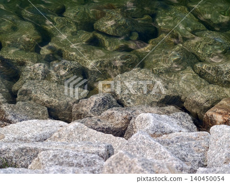 Granite shoreline rocks with clear green water and rippling reflections 140450054