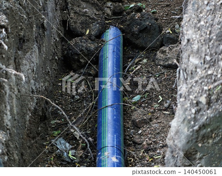 Blue water pipe laid in narrow soil trench between rocks Blue water pipe laid in narrow soil trench between rocks 140450061