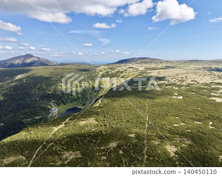 Wide mountain plateau with trails alpine lake and distant peaks under blue sky Wide mountain plateau with trails alpine lake and distant peaks under blue sky 140450110