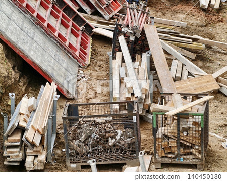 Construction site stacked lumber, metal formwork and hardware in soil 140450180
