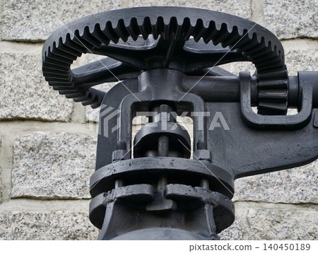 Close-up of industrial cast iron gear and mechanism against stone wall Close-up of industrial cast iron gear and mechanism against stone wall 140450189