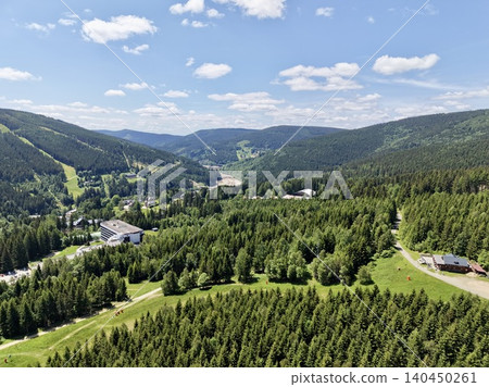 Aerial view of green mountain valley with forested slopes and scattered buildings 140450261