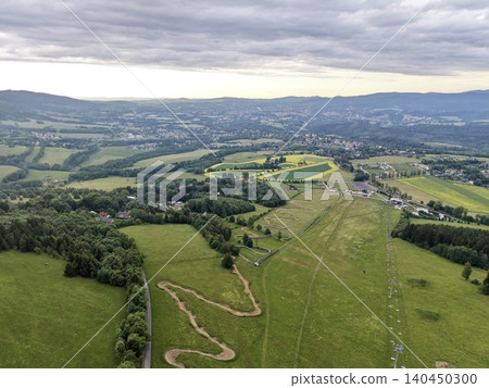 Aerial view of rolling countryside with fields and forest under cloudy sky Aerial view of rolling countryside with fields and forest under cloudy sky 140450300