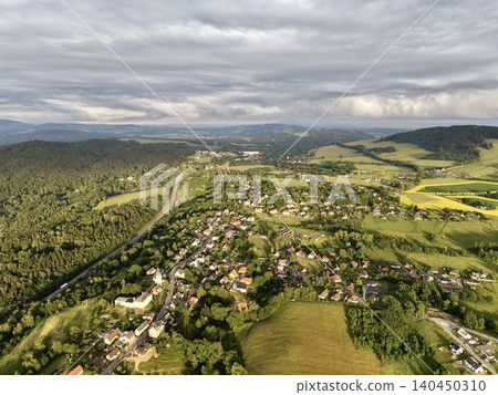 Aerial view of rural village nestled in green rolling hills under cloudy sky 140450310