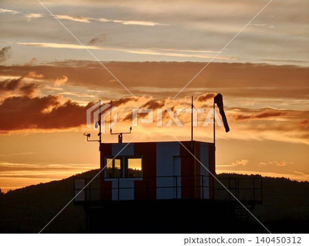 Control tower silhouette with wind sock at sunset over low hills Control tower silhouette with wind sock at sunset over low hills 140450312