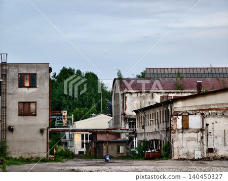 Abandoned industrial buildings with overgrown courtyard and cloudy sky Abandoned industrial buildings with overgrown courtyard and cloudy sky 140450327