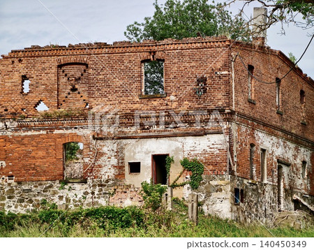Weathered red brick farmhouse ruin with overgrown vegetation 140450349