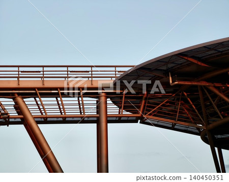 Modern steel pedestrian bridge and covered walkway structure against pale sky Modern steel pedestrian bridge and covered walkway structure against pale sky 140450351