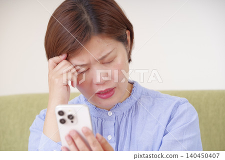 A woman looking at her smartphone, lost in thought and looking anxious. A woman looking at her smartphone, lost in thought and looking anxious. 140450407